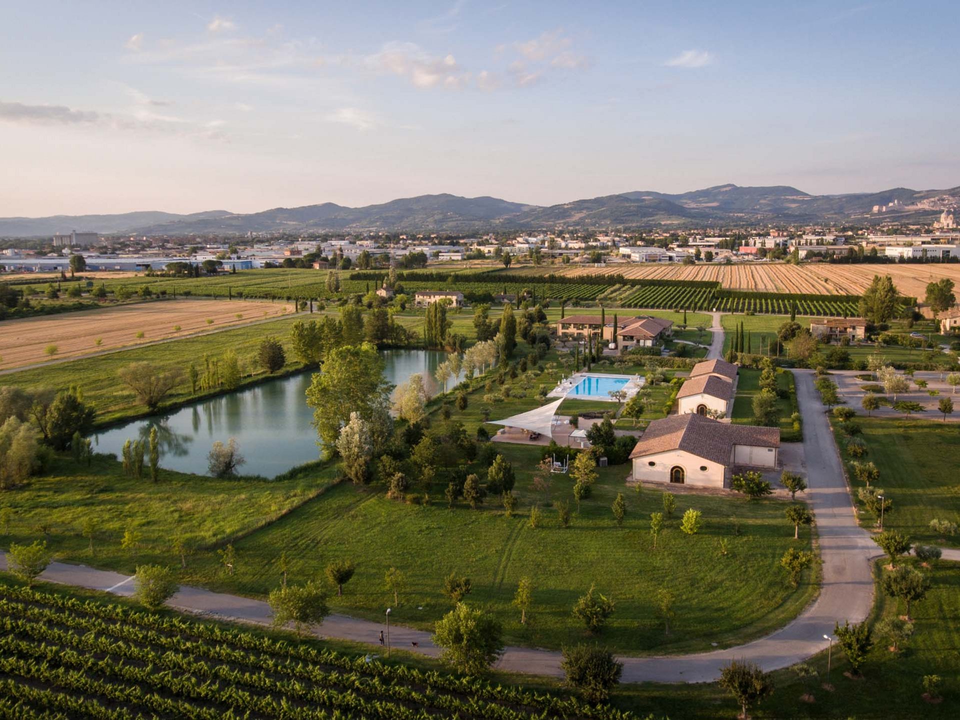 La missione di Valle di Assisi Veduta aerea di un agriturismo con piscina, laghetto e campi coltivati