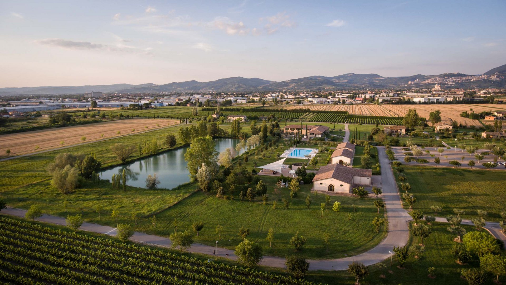 A hotel in Assisi and its owners Aerial view of a farmhouse with pool, pond, and cultivated fields