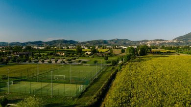 Vacanza vicino ad Assisi, Resort Hotel com Campo da Padel Tennis Bike Hotel 3 piscine campo da calcetto. Campi sportivi verdi vicino a campi gialli e colline sotto un cielo azzurro