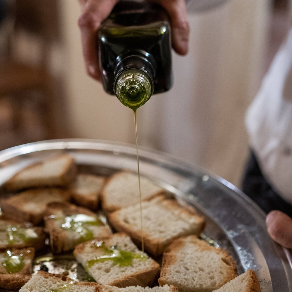 Discover our farm in Umbria. Oil being poured onto bread slices on a tray
