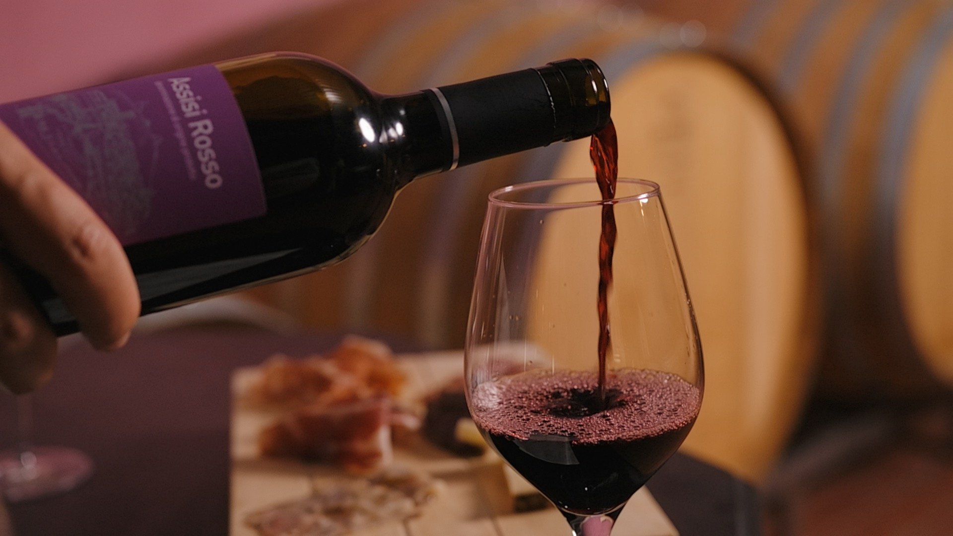 At Valle di Assisi, our restaurant, Recanto, awaits you. Red wine being poured into glass with wooden barrels in background