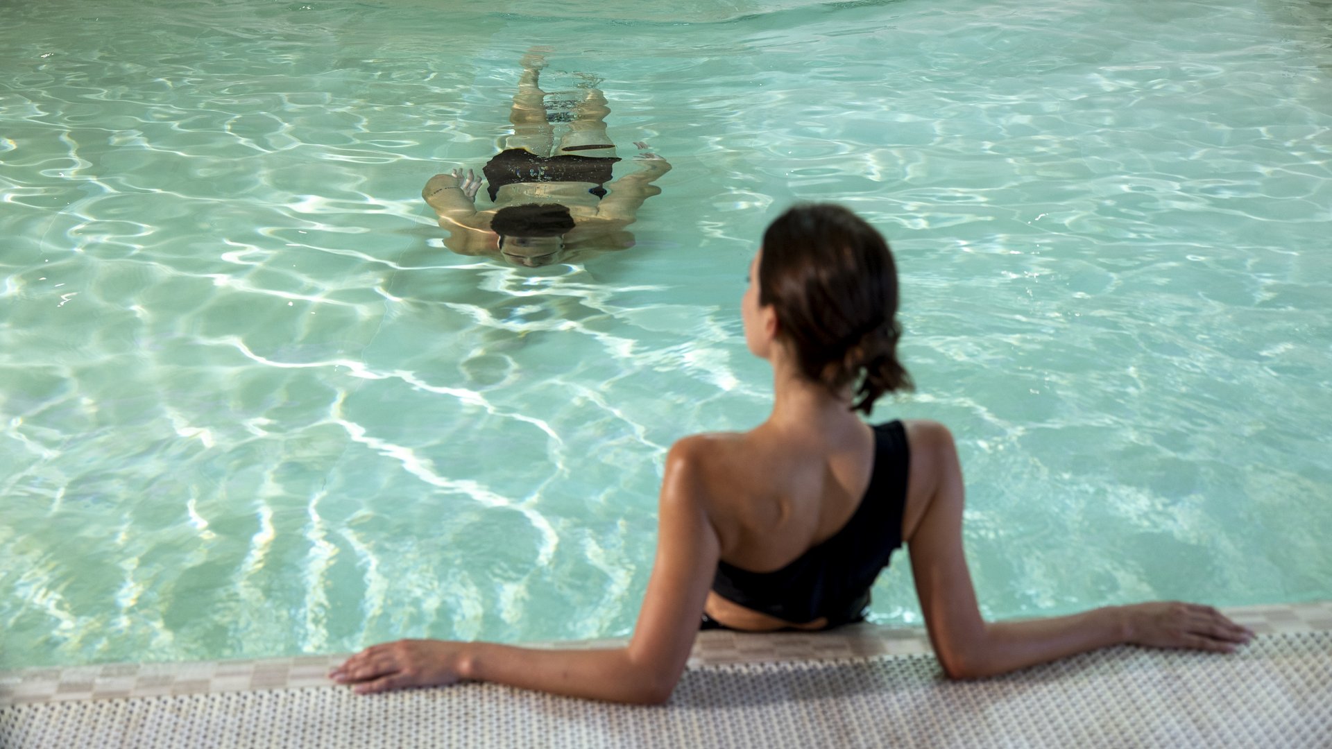 Hotel mit Wellness: Valle di Assisi Frau im schwarzen Badeanzug entspannt am Poolrand, andere Person schwimmt