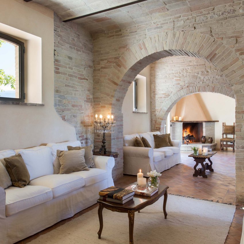 Un resort vicino ad Assisi indimenticabile Soggiorno rustico con archi in mattoni, divani bianchi e camino acceso