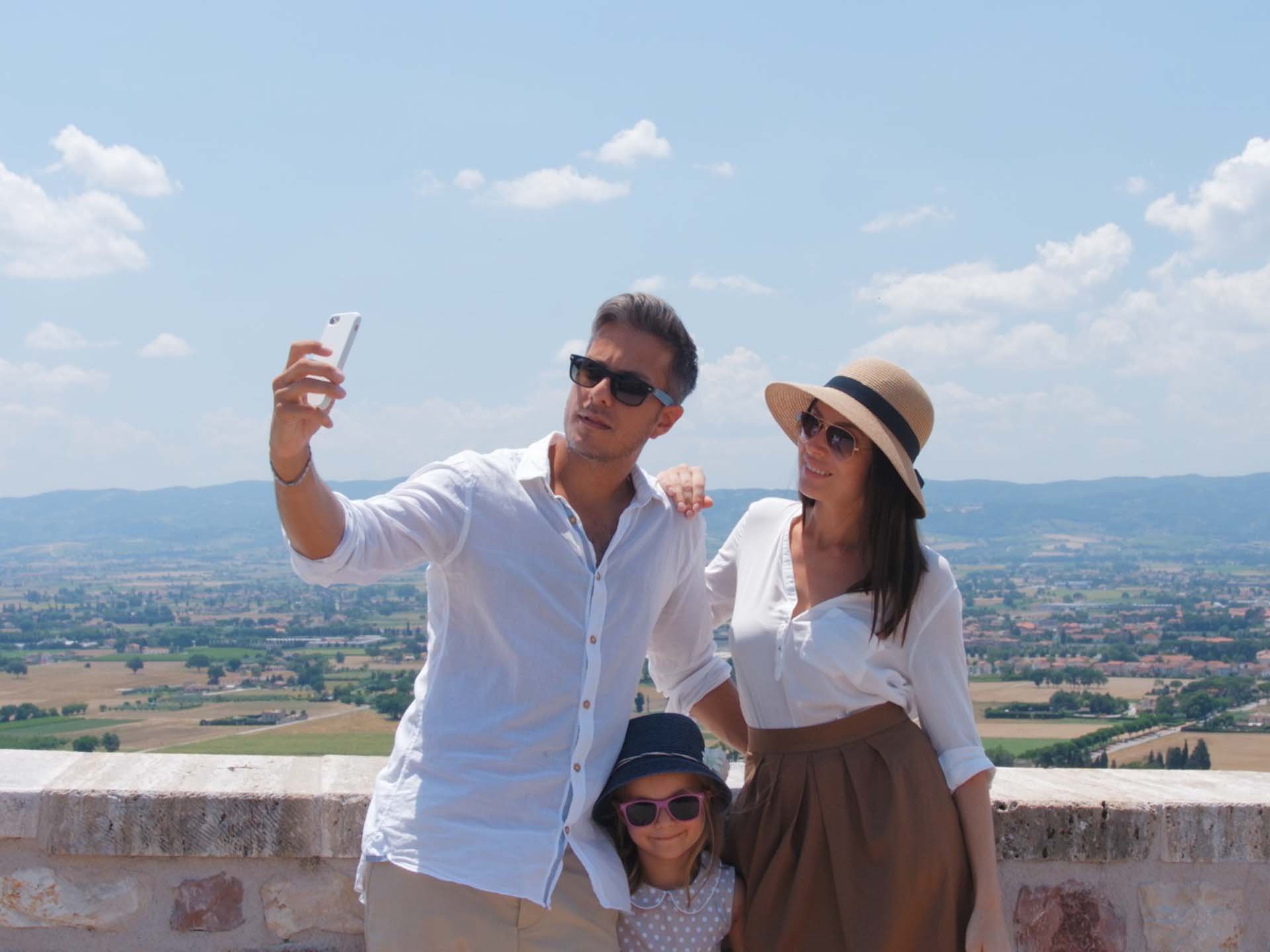 La missione di Valle di Assisi Famiglia in vacanza che si fa un selfie con panorama rurale dietro