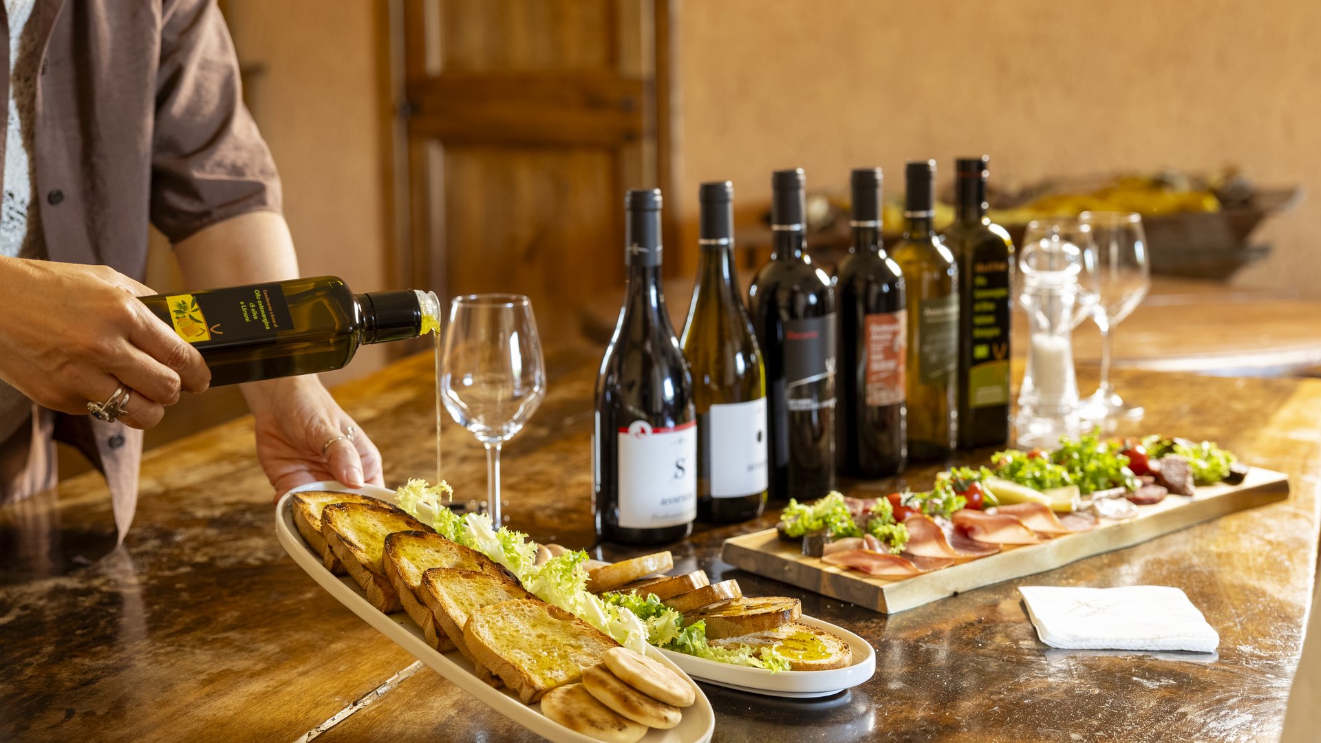 Team building in un hotel con centro benessere in Umbria Persona che versa olio d'oliva su pane tostato con bottiglie di vino sul tavolo