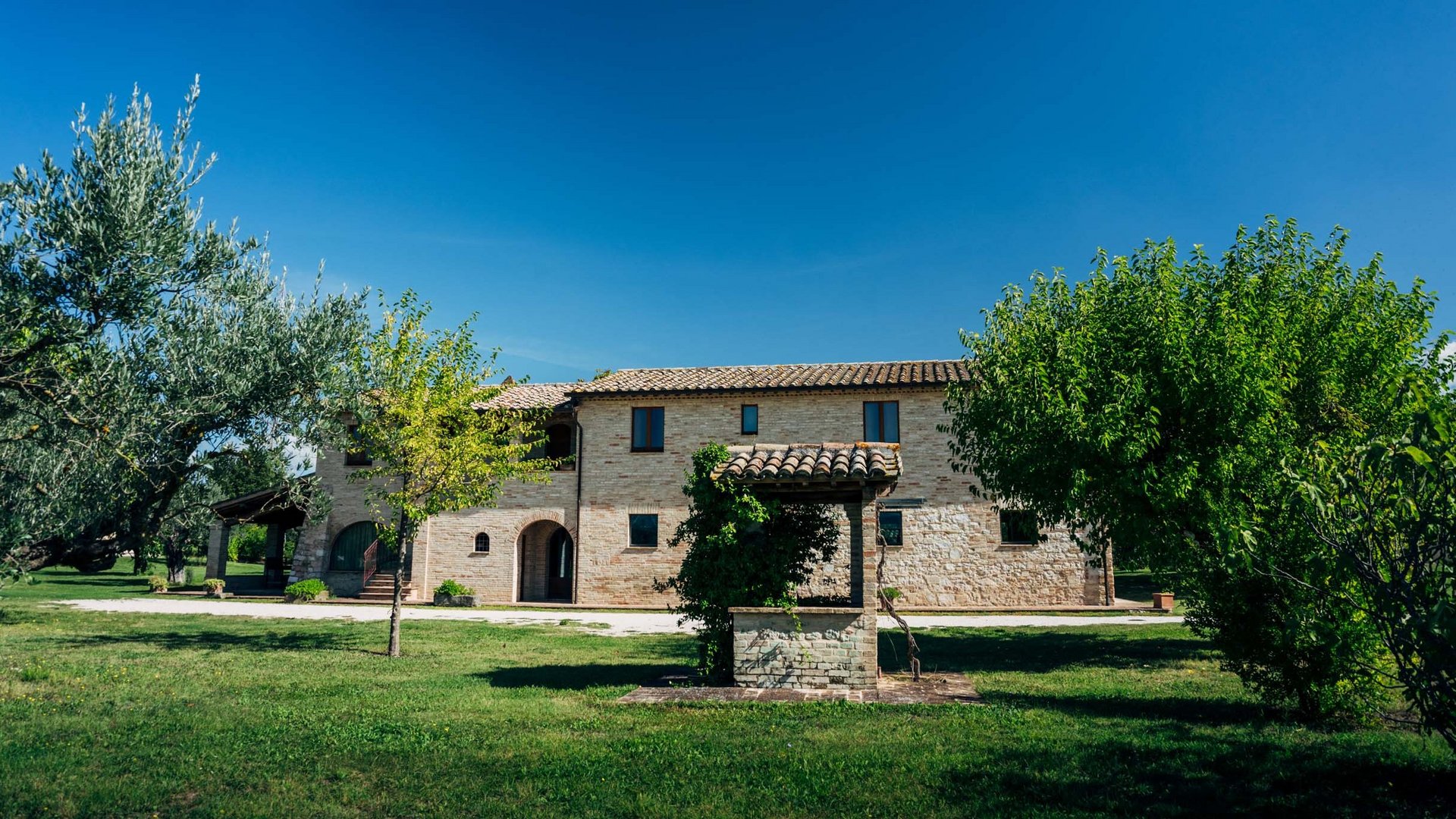 Villa ad Assisi con piscina privata, vacanze nel cuore dell'Umbria Casa di campagna con pozzo e alberi sotto un cielo terso