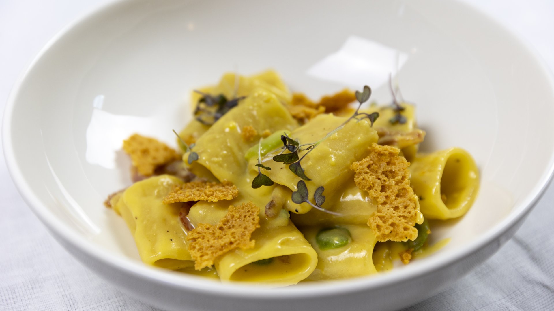 At Valle di Assisi, our restaurant, Recanto, awaits you. Short pasta with creamy sauce, fresh herbs, and crispy bread pieces in white bowl