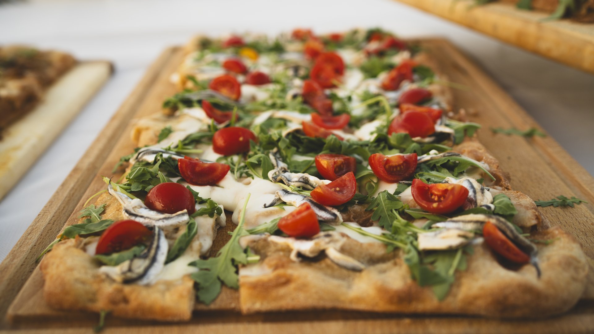 Umbrien: Unterkunft mit Restaurant Rechteckige Pizza mit Kirschtomaten, Rucola und Mozzarella auf Holzbrett