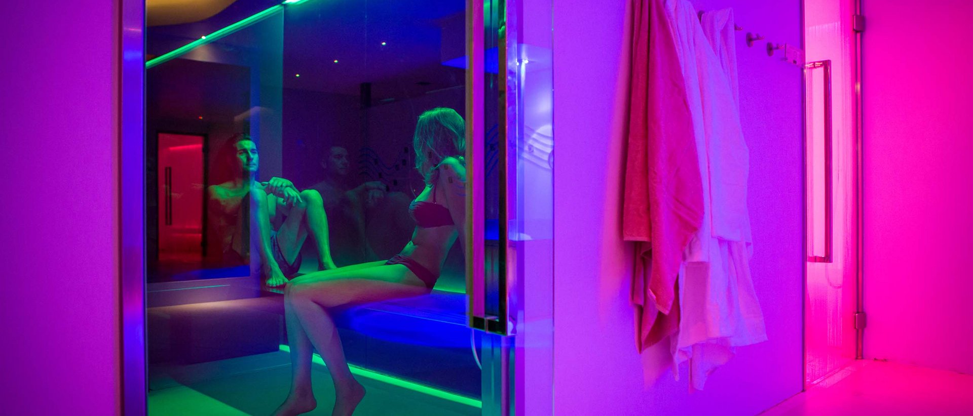 Offerte Last Minute SPA Umbria Due persone sedute in una sauna con illuminazione colorata e accappatoi appesi