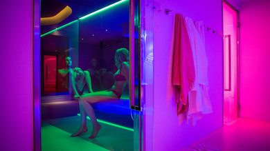 Hotel mit Wellness: Valle di Assisi Zwei Personen sitzen in einer Sauna mit bunter Beleuchtung und hängenden Handtüchern