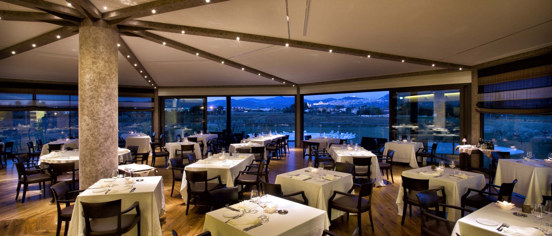 At Valle di Assisi, our restaurant, Recanto, awaits you. Elegant restaurant with set tables and evening panoramic view.