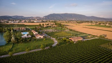 Perugia ha un Centro Meeting e Congressi d'eccezione: ai piedi di Assisi in Umbria Veduta aerea di una fattoria con campi coltivati e montagne sullo sfondo
