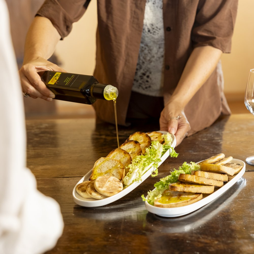 Hotel con ristorante vicino ad Assisi: benvenuti al Recanto Persona versa olio d'oliva su fette di pane tostato con insalata su piatti bianchi