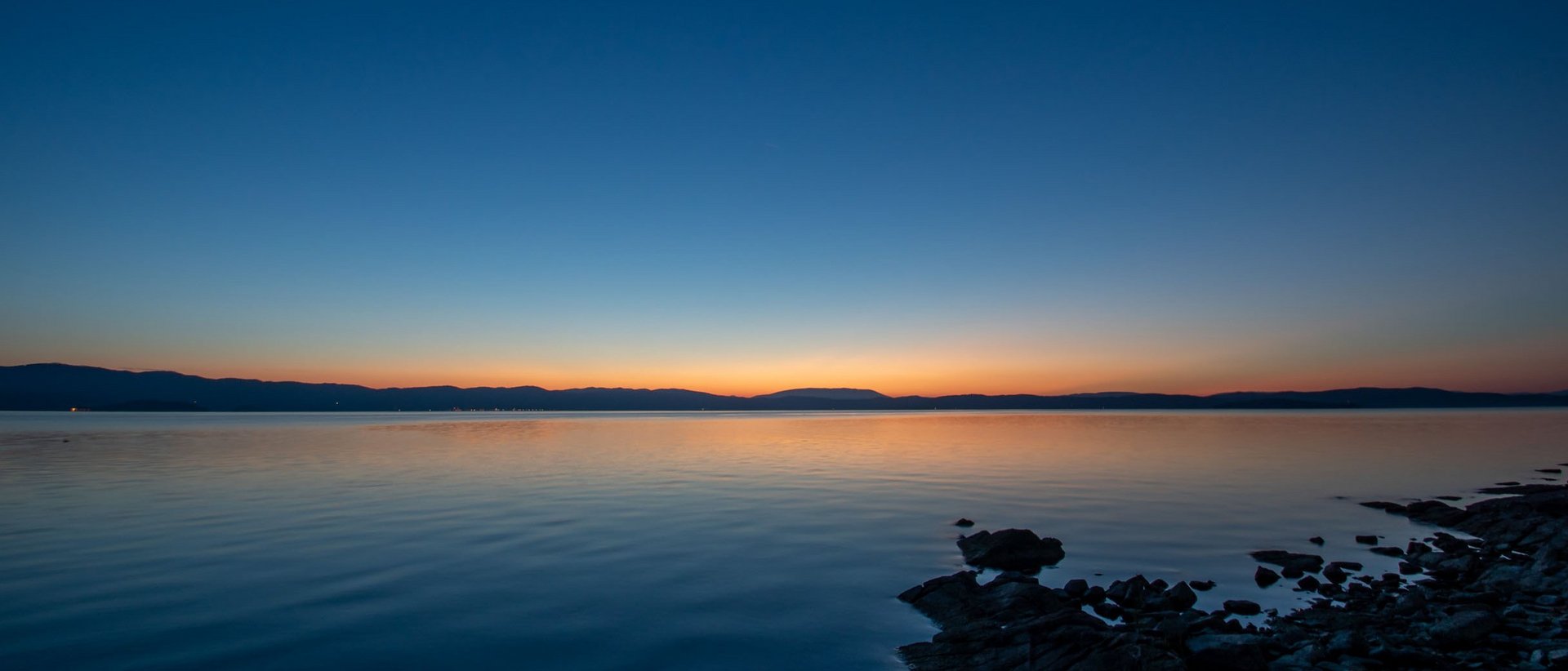 Sehenswürdigkeiten in Assisi und Umgebung Sonnenuntergang am See mit klarem Himmel und Spiegelungen auf ruhigem Wasser
