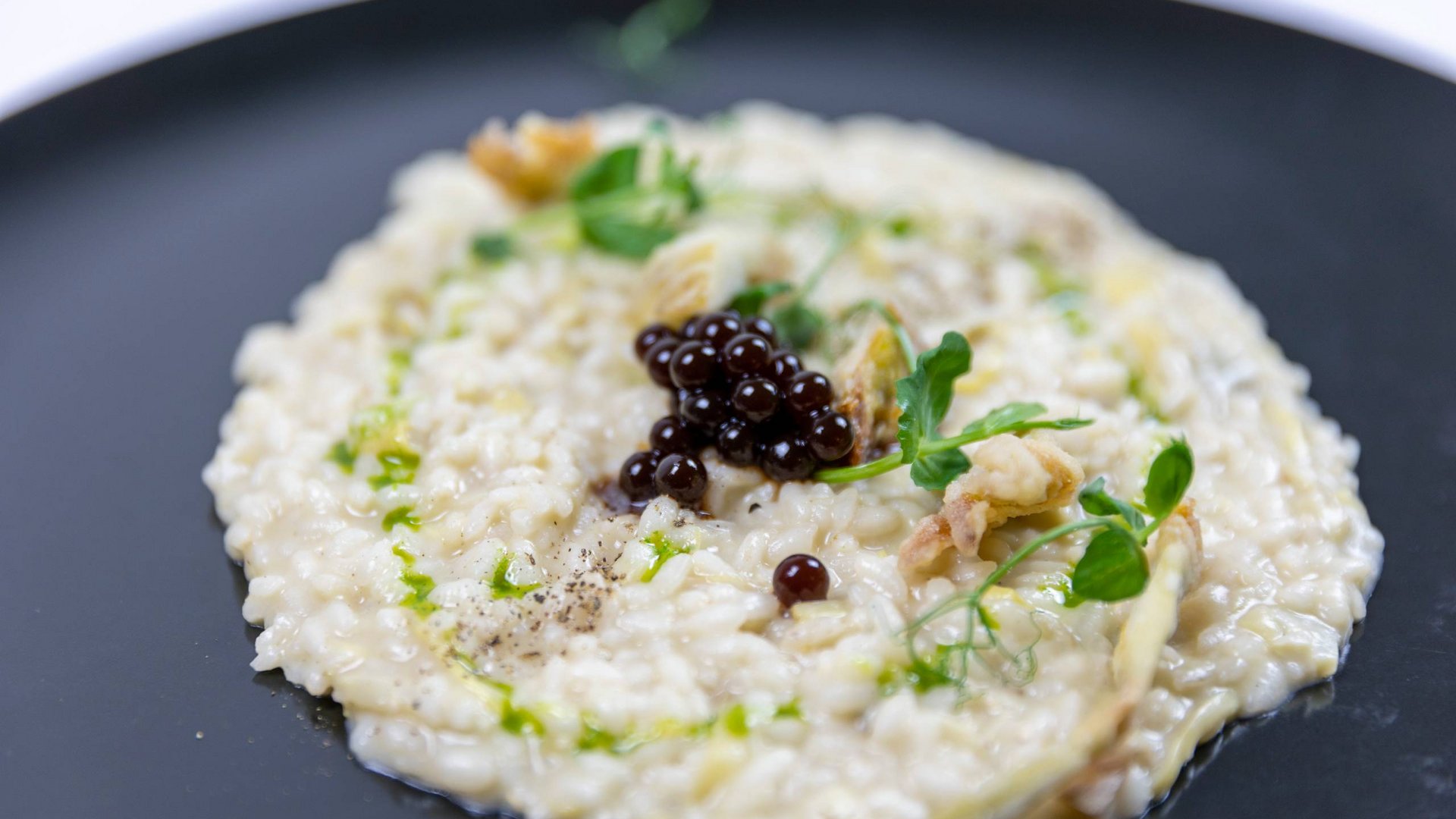 A holiday near Assisi: activities galore Creamy risotto topped with black gel spheres and fresh herbs on a black plate